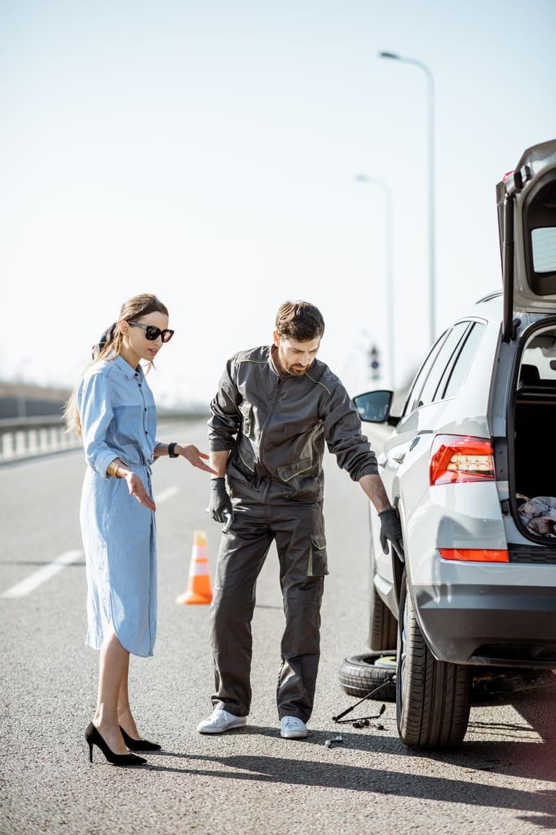 Worker with woman near the broken car on the highway providing roadside assistance